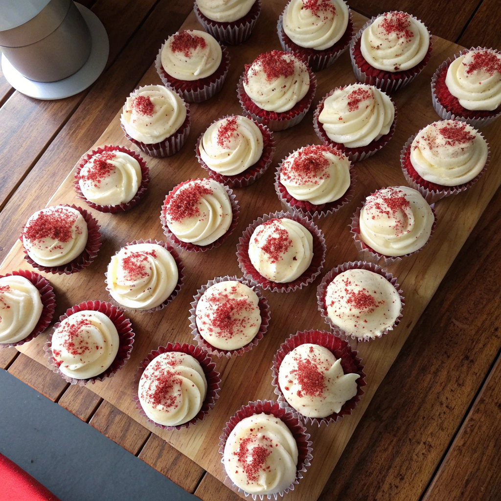 Red velvet cupcakes with cream cheese frosting, showcasing textured peaks and red crumb garnish, in rustic grid display.